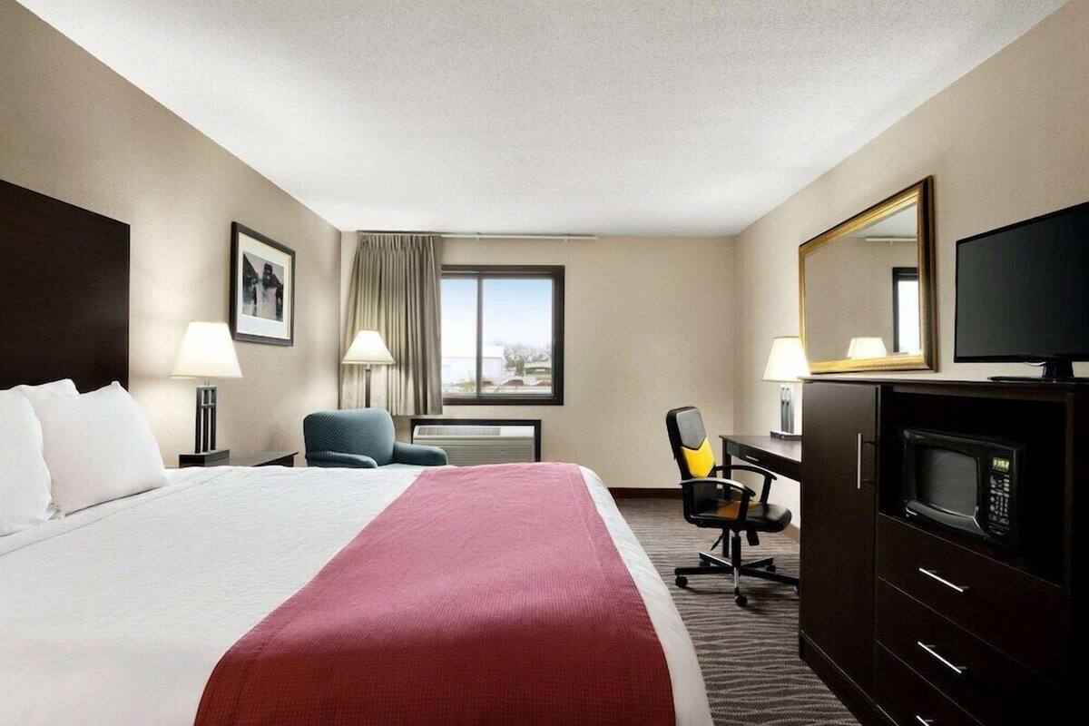 Een hotelkamer met een bed, bureau, stoel, televisie en een grote spiegel.
