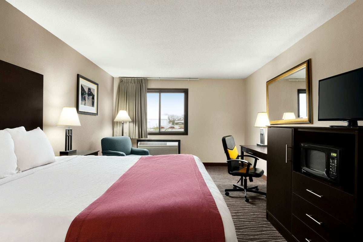Een hotelkamer met een bed, bureau, stoel, televisie en magnetron.