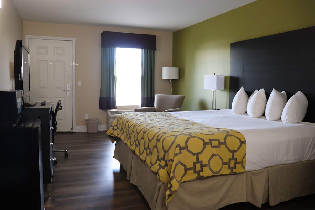 Een hotelkamer met een bed, bureau, stoel, lamp en raam met gordijnen.