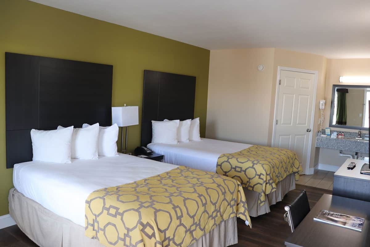 Hotelkamer met twee bedden, een bureau, een stoel, een badkamer met spiegel en een klok aan de muur.