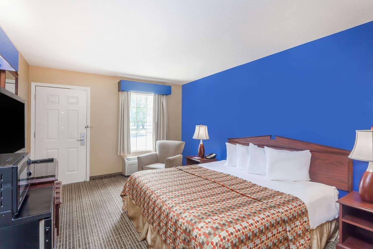 Een hotelkamer met een bed, een stoel, een bureau, een televisie en een raam met gordijnen.