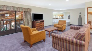 Habitación de hotel con televisión, sofá, sillón y vistas a un balcón con sillas.