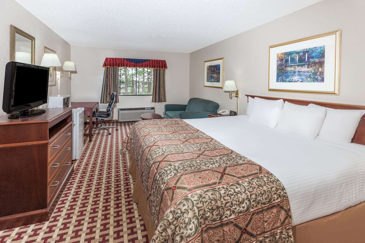 A hotel room with a large bed, a desk with a television, a chair, a desk lamp, and a window with curtains.