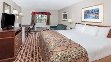 Una habitación de hotel con una cama grande, un escritorio con televisor, una silla, una lámpara de escritorio y una ventana con cortinas.