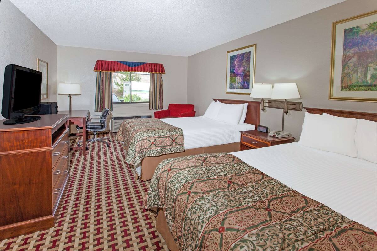 A hotel room with two beds, a desk with a television, a chair, a desk lamp, and a window with curtains.