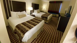 Habitación de hotel con dos camas, un escritorio, una silla, una lámpara, un televisor y una alfombra estampada.