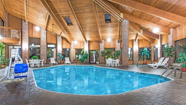Una piscina interior con techo de madera, paredes de ladrillo y sillones blancos alrededor.