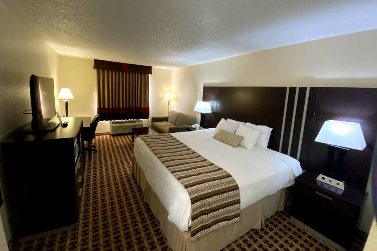 A hotel room with a large bed, a desk, a chair, two bedside lamps, and a patterned carpet.
