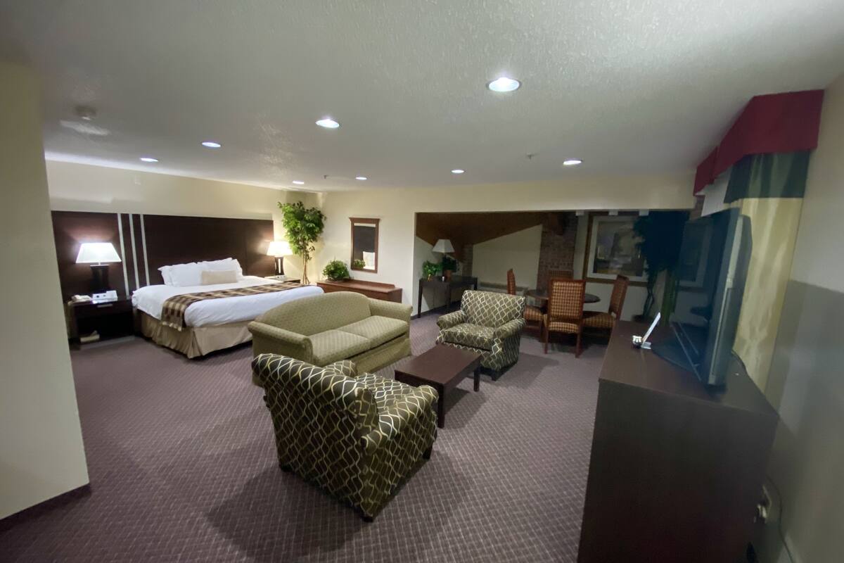 A hotel room with a bed, two sofas, a coffee table, a desk with a computer, and a TV.