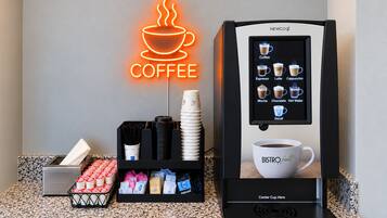 A coffee machine with a selection menu, disposable cups, and a neon coffee sign.