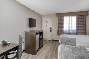 Habitación de hotel con cama, escritorio, teléfono, televisión y puerta con un cartel.