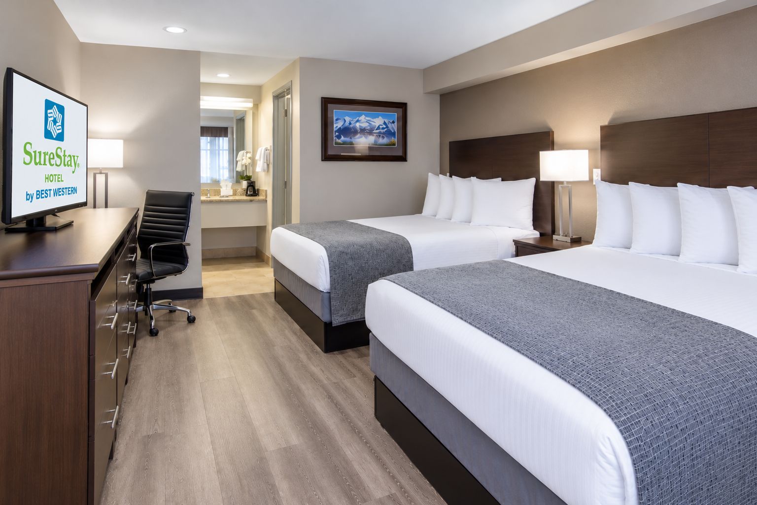 A hotel room with two beds, a desk, a chair, a television, and a framed picture on the wall.