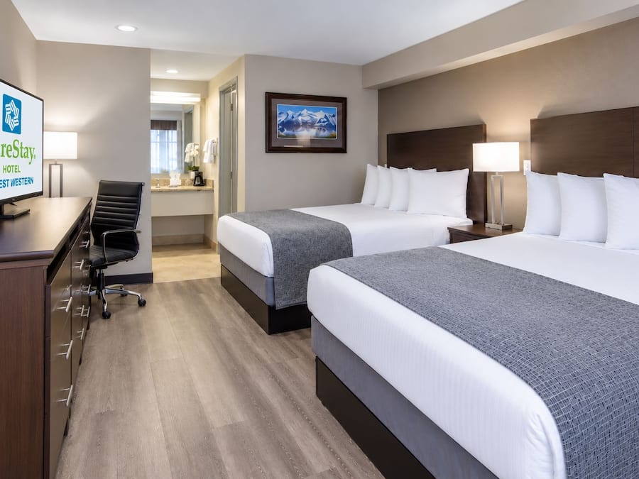 A hotel room with two beds, a desk, a chair, a television, and a framed picture on the wall.