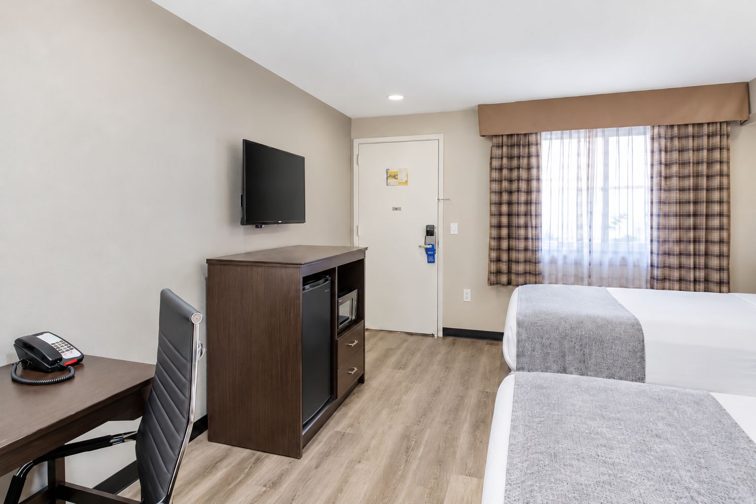 A hotel room with a bed, a desk with a telephone, a television, and a door with a keycard reader.