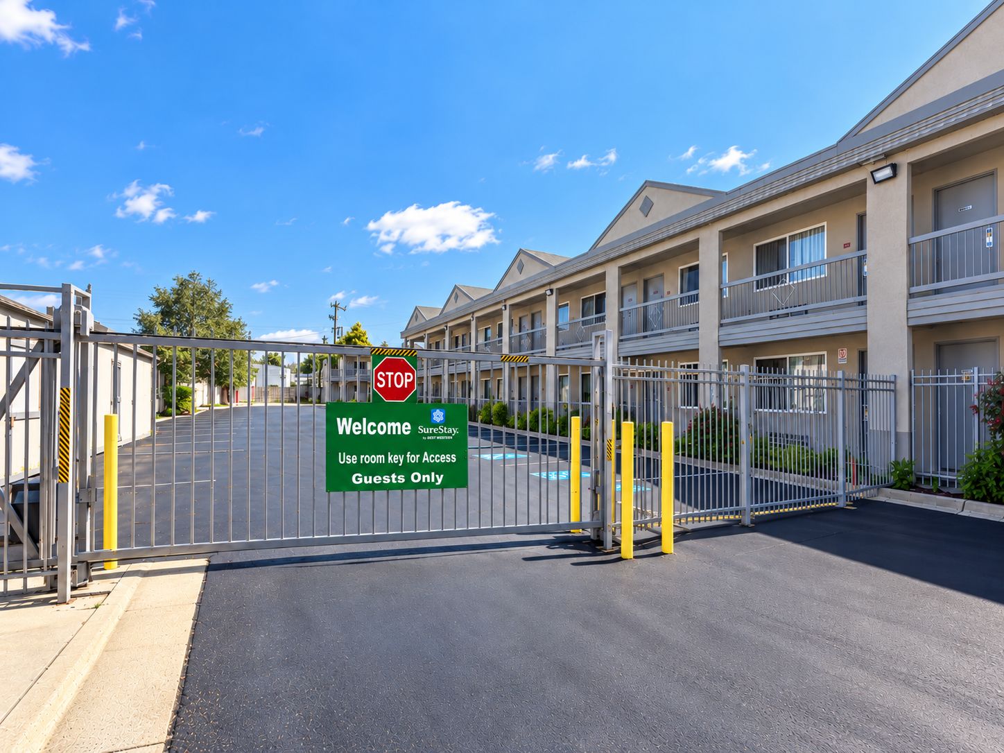 A gated entrance to a hotel with a 'Welcome' sign, a 'Stop' sign, and a 'Use room key for Access Guests Only' sign.
