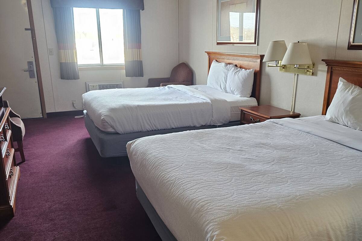 Ein Hotelzimmer mit zwei Betten, einem Fenster mit Vorhängen, einer Wandlampe und einer Tür.