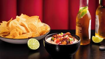 Un tazón de guacamole, totopos y una botella de cerveza Corona sobre una mesa.