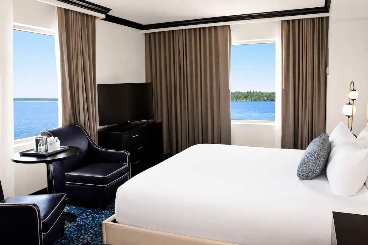 A hotel room with a large bed, a TV, a desk with a tray of items, and a view of the water.