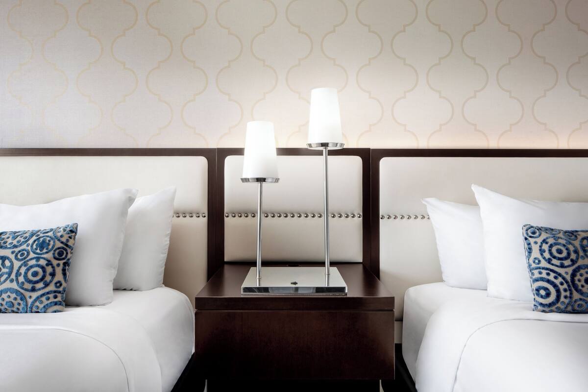 A hotel room with two beds, a nightstand, and a wall with a geometric pattern.