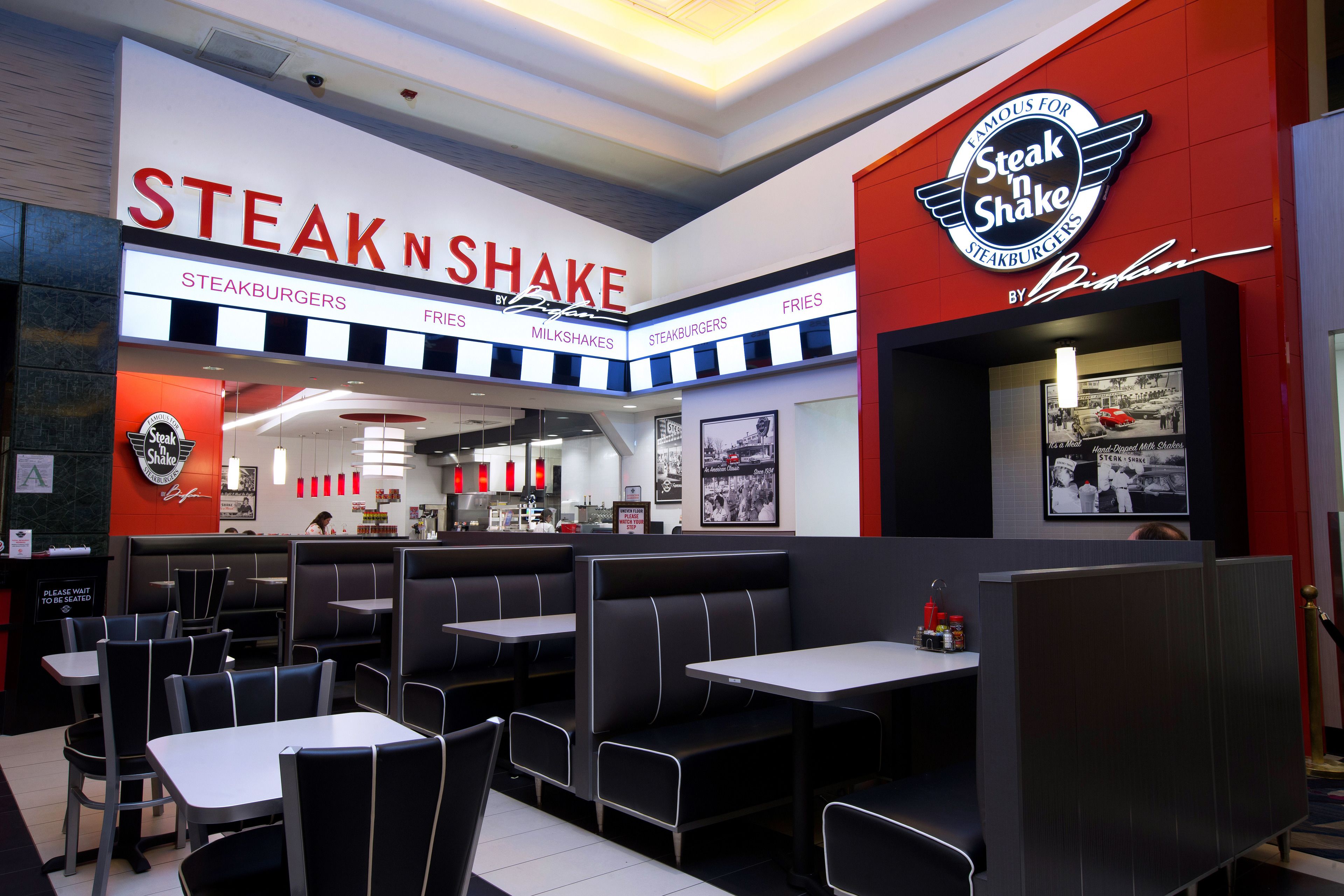 Ein Restaurantinneres mit Sitzecken und Tischen, einer Theke mit Speisekarte und einem großen Schild mit der Aufschrift "Steak 'n Shake".