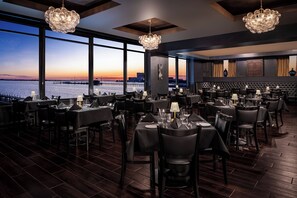 Un restaurante con mesas dispuestas para comer, amplias ventanas con vista al agua y un candelabro.