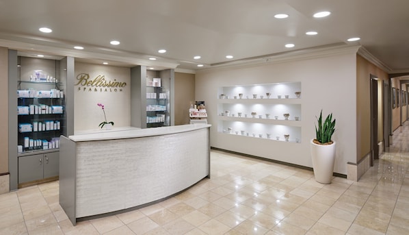 A reception area with a white reception desk, shelves with products, and a wall with a 'Bellissimo' sign. - Harrah's Gulf Coast Hotel & Casino - A Caesars Rewards Destination (Biloxi)