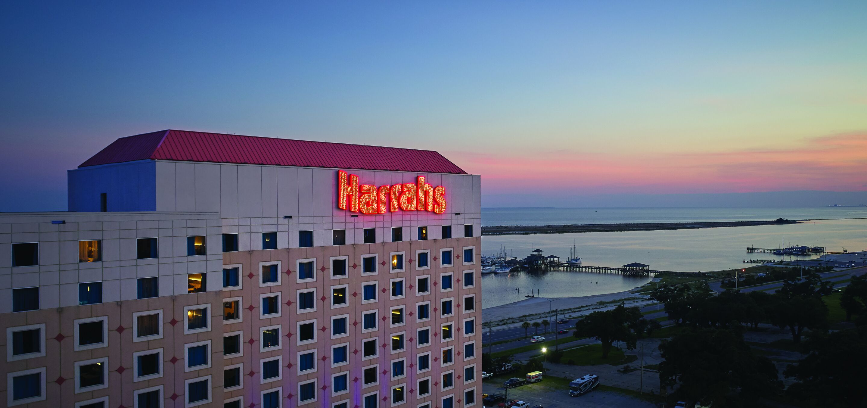 A hotel with a prominent Harrah's sign, a waterfront view, and a dock area.
