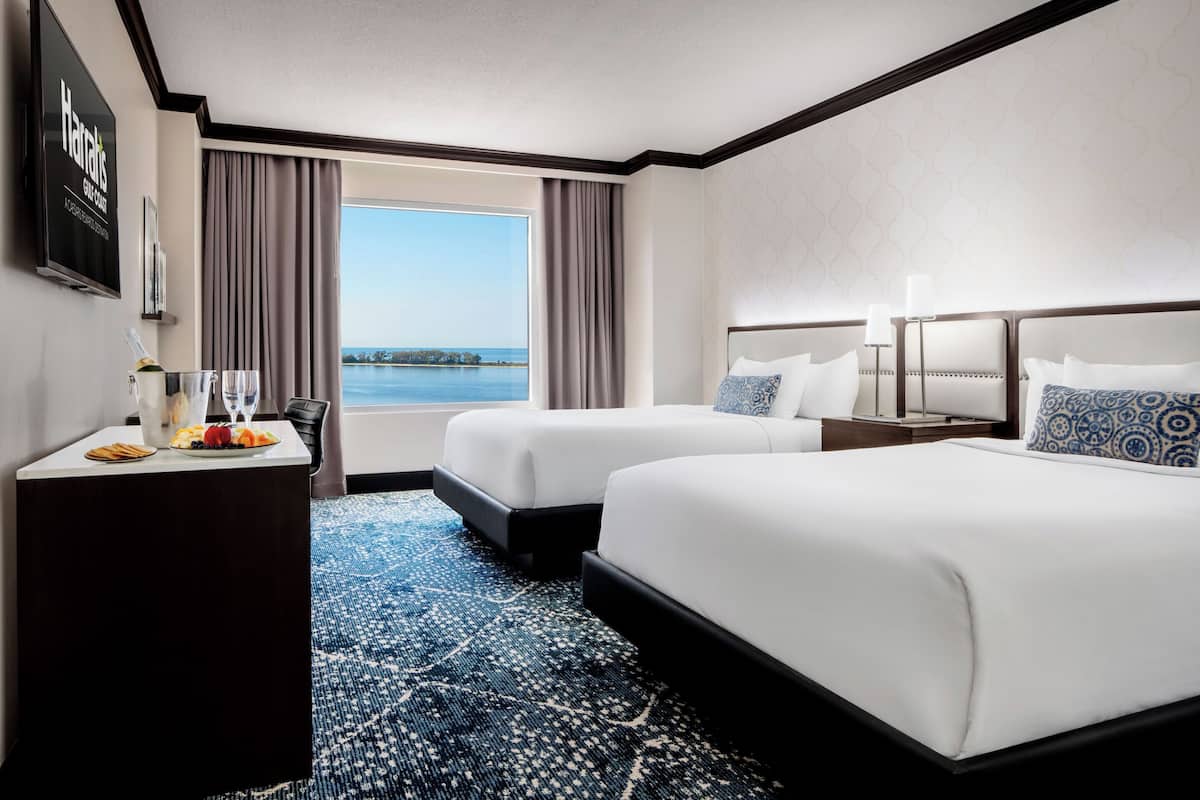 A hotel room with two beds, a desk with a bottle of champagne, and a view of the water.