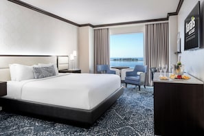Une chambre d’hôtel avec un lit, un bureau sur lequel se trouvent une bouteille et des verres, une chaise, et une vue sur la mer.