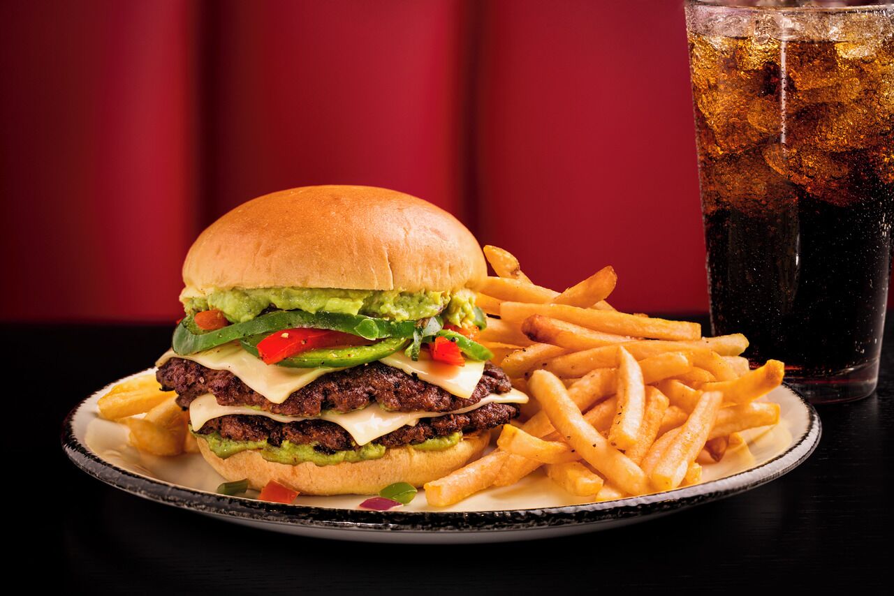 A burger with fries and a soda on a plate.