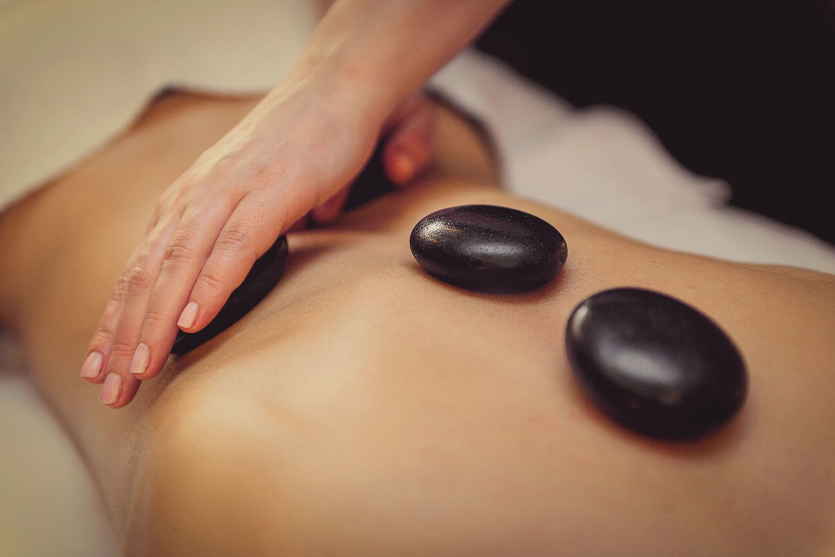 Gros plan d’un massage effectué à l’aide de deux pierres noires sur le dos d’une personne.