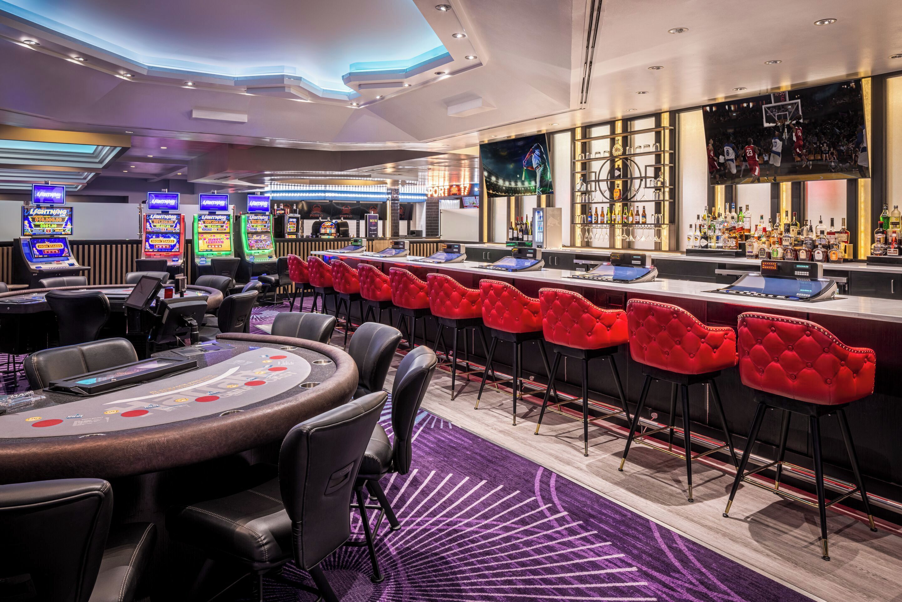 A casino with blackjack tables, red bar stools, slot machines, and a bar area.