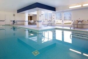 An indoor swimming pool with clear blue water, tiled walls, and windows offering views of the outside.