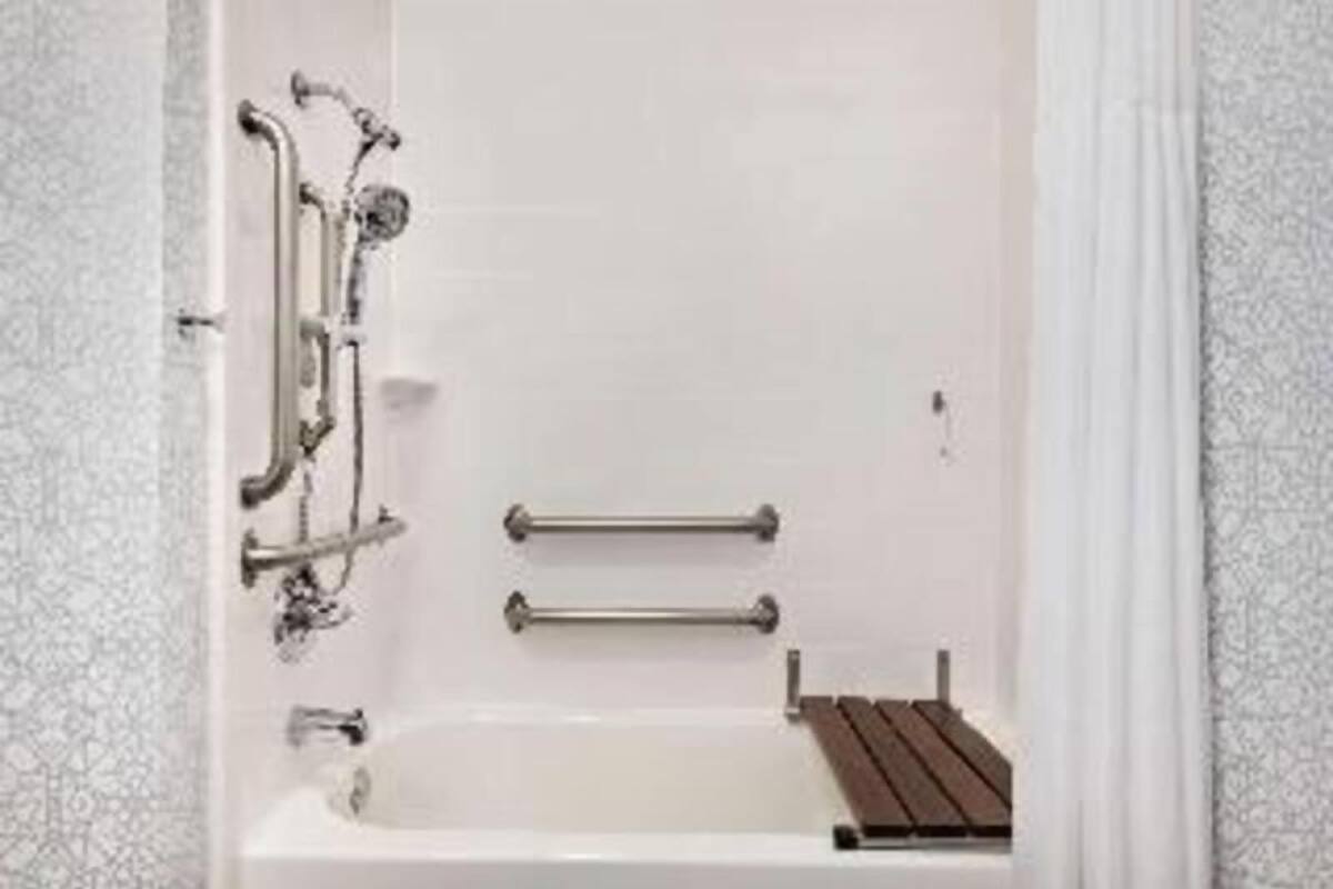 A bathtub with grab bars, a showerhead, and a wooden shelf.
