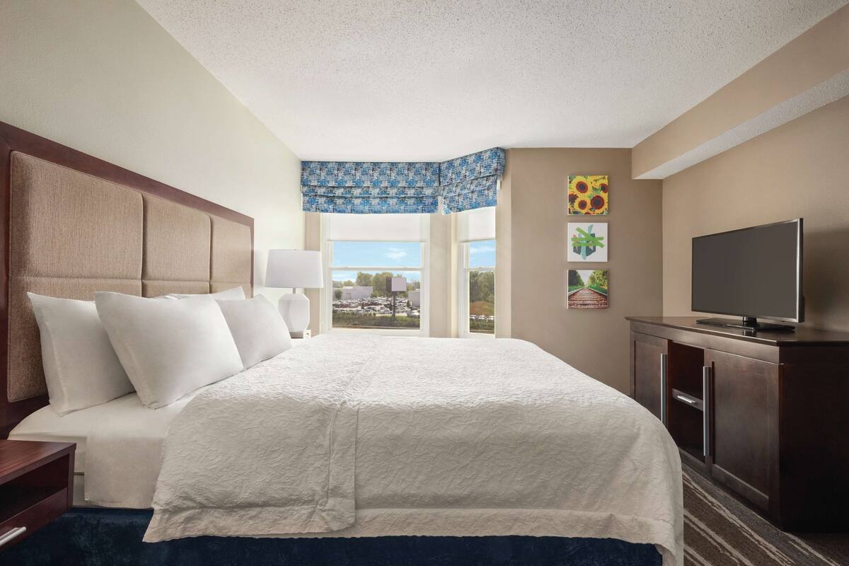 A hotel room with a large bed, a TV, a desk, and a window with a view of the city.