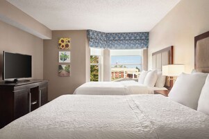 A hotel room with two beds, a TV, and a window with a view of buildings and trees.