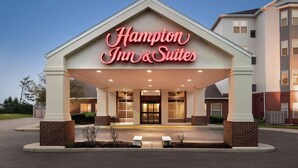 A Hampton Inn & Suites hotel entrance with a covered walkway, brick pillars, and a clear sky.