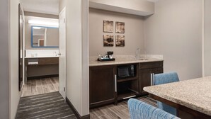 A compact hotel room with a kitchenette, a small dining area, and a bathroom with a mirror and towel rack.