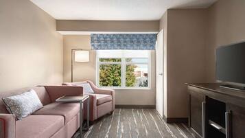 Un hotel moderno con sofá, dos sillones, una mesita, televisor y ventana con vistas a árboles y edificios.
