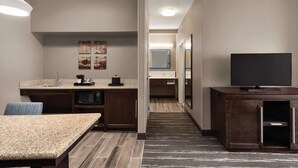 A compact hotel room with a kitchenette, a dining area, a TV, and a mirror.
