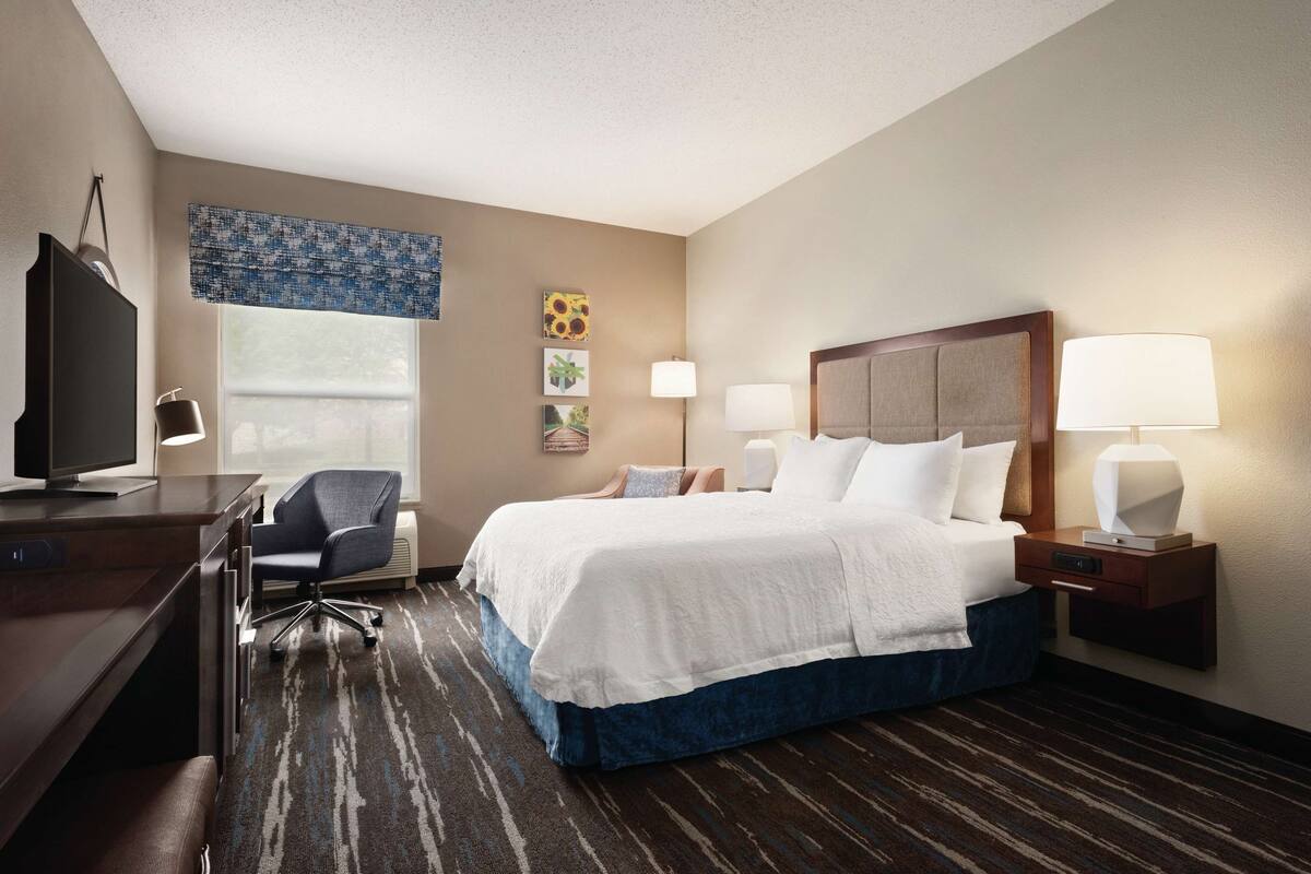 A hotel room with a large bed, a desk with a computer, a chair, and a TV.