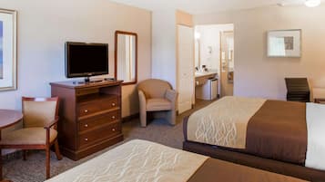 A hotel room with two beds, a desk with a television, a dresser, a chair, and a bathroom visible through an open door.