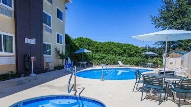 A pool area with two hot tubs, lounge chairs, and umbrellas.