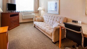 A hotel room with a sofa, a desk, a television, a lamp, and a framed picture on the wall.