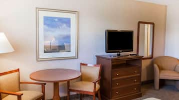 Habitación de hotel con una mesa redonda, dos sillas, un televisor sobre un mueble de madera, un espejo y un cuadro en la pared.