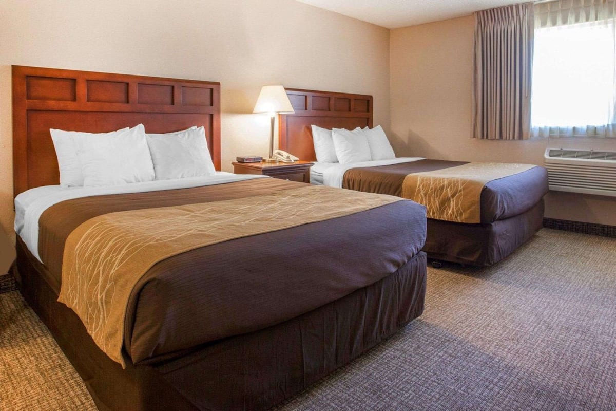 Quarto de hotel com duas camas, mesa de cabeceira com abajur, telefone e aparelho de ar condicionado.