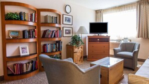 A hotel room with a large bookshelf, a flat-screen TV, a comfortable armchair, a sofa, and a wooden coffee table.