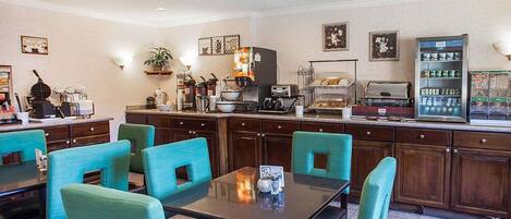A hotel dining area with teal chairs, a buffet counter, and various kitchen appliances.
