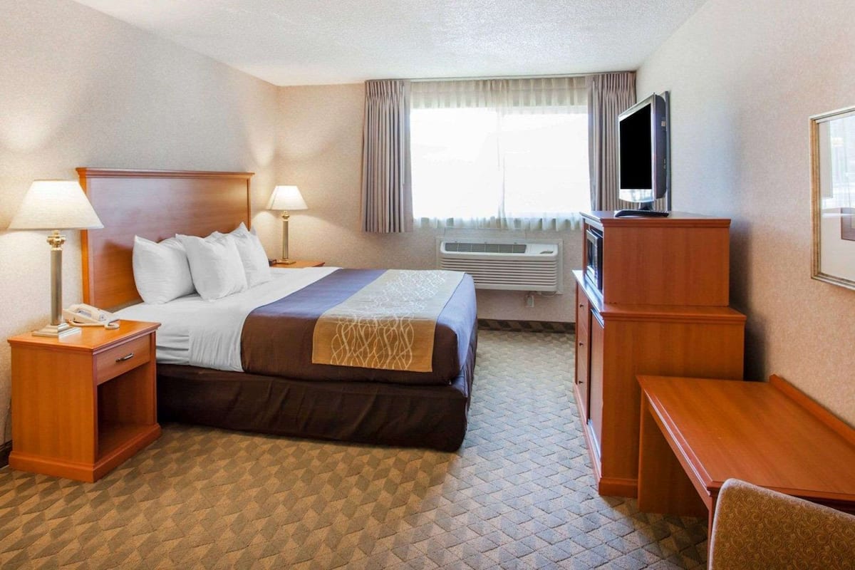 Quarto de hotel com cama, abajures, escrivaninha, televisão e ar condicionado.