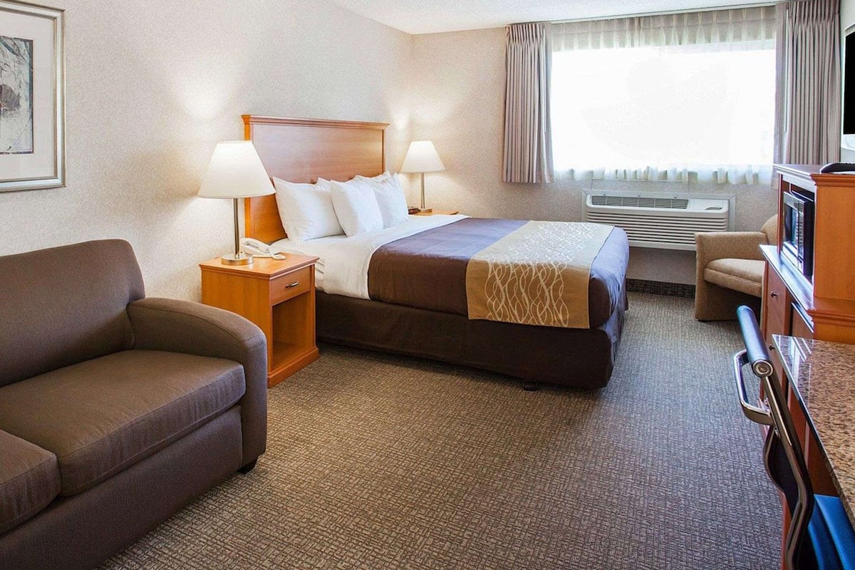 Quarto de hotel com cama, duas luminárias de cabeceira, sofá, televisão e aparelho de ar condicionado.